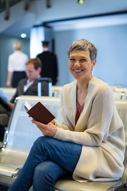 Foto gratuita ritratto di donna sorridente con passaporto seduto nella zona di attesa