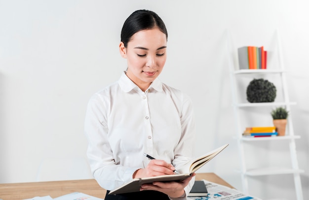 Portrait of a smiling young asian businessman writing on diary with pen