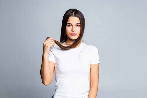 Portrait of smiling young beautiful woman holding ends of her long brown hair on white