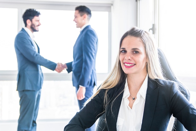 Portrait of smiling young businesswoman in front of men shaking hands