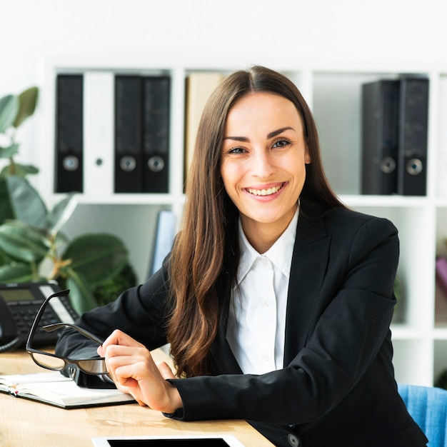 Portrait of a smiling young businesswoman holding eyeglasses in hand looking at camera