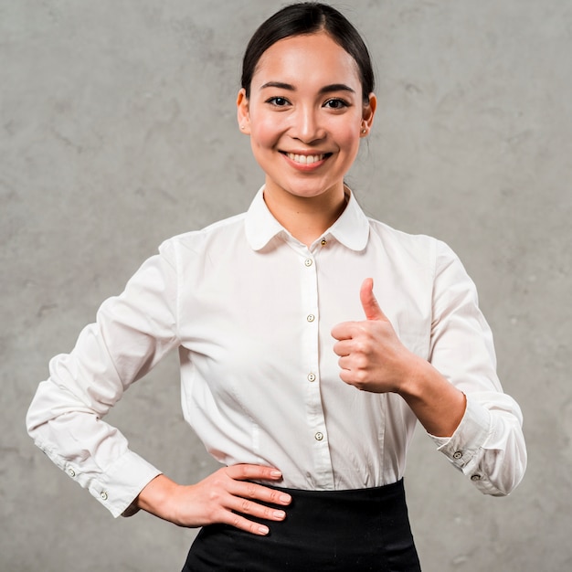Portrait of a smiling young businesswoman with hand on her hips showing thumb up sign