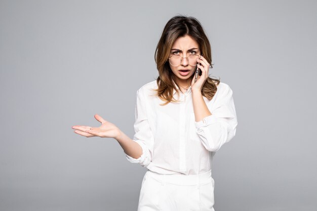 Portrait of a smiling young casual woman talking on mobile phone isolated over white wall