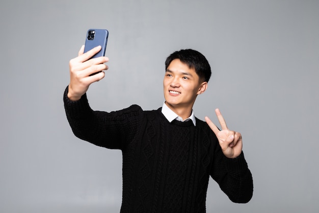 白い壁に分離されている間携帯電話でselfieを取って笑顔の若い中国人男性の肖像画
