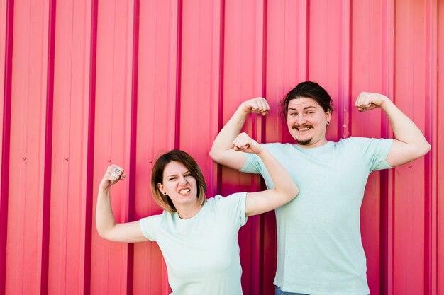 Portrait of a smiling young couple flexing their arms against corrugated iron sheet