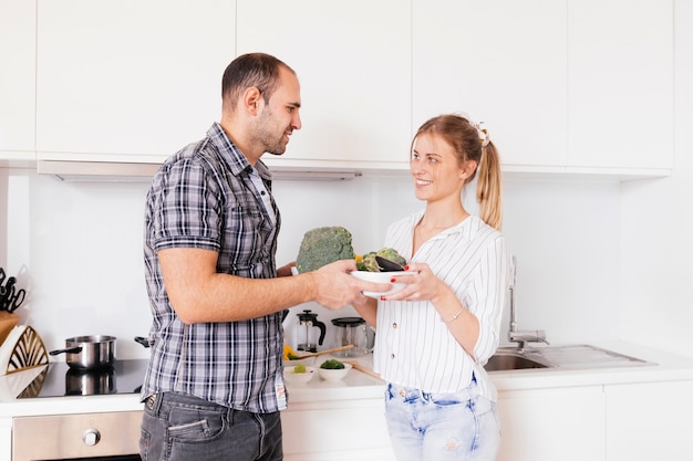 Portrait of a smiling young couple holding bowl of raw vegetables in hands
