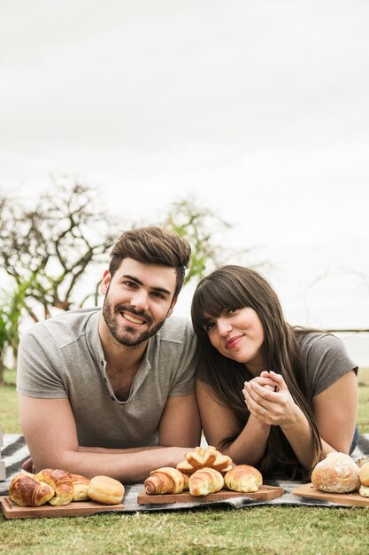 Portrait of smiling young couple lying on blanket with baked bread on wooden tray