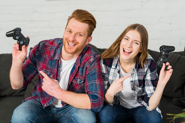 Portrait of a smiling young couple pointing finger toward the video game controller