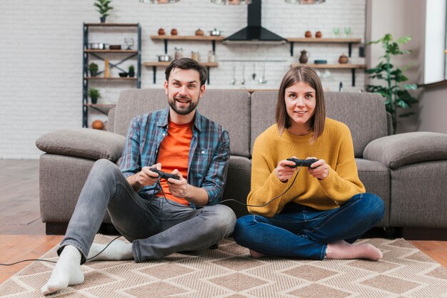 Portrait of smiling young couple sitting on floor playing the video game