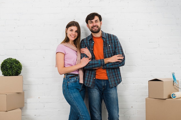 Free photo portrait of smiling young couple standing in front of white wall looking to camera