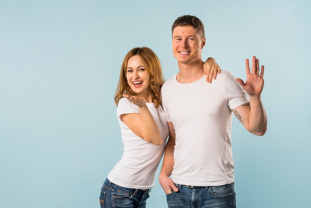 Portrait of a smiling young couple waving hands against blue background