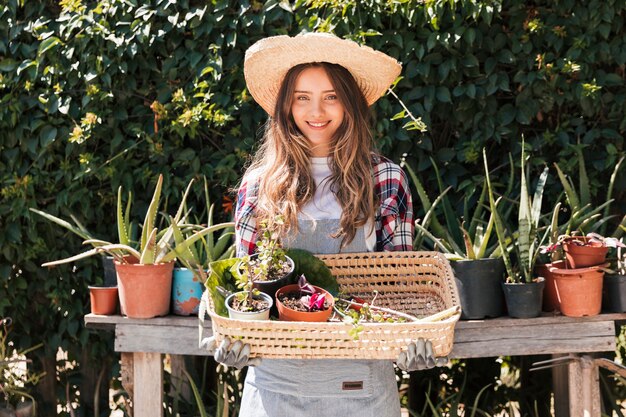 バスケットに鉢植えの植物を保持している笑顔の若い女性庭師の肖像画