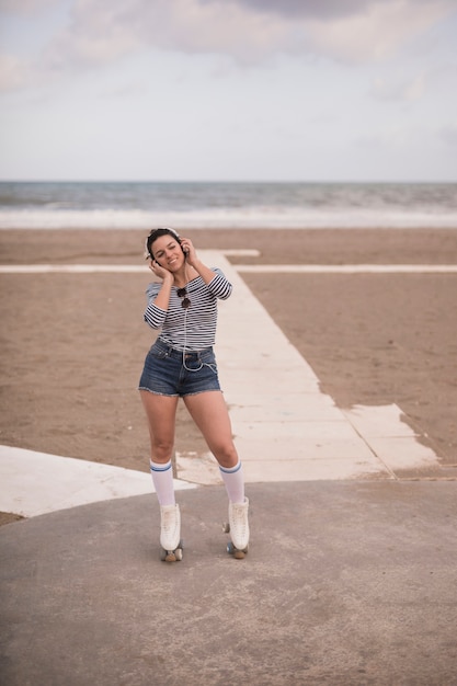 Portrait of a smiling young female skater listening music on headphone at beach