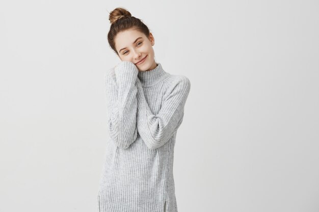 Portrait of smiling young female  with lovely gaze. Pretty girl 20s bending her head to hands folded on chest taking pleasure being alone. Beauty and loneliness concept