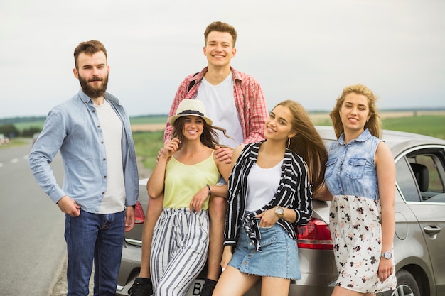 Портрет улыбающиеся молодые друзья, стоя рядом с автомобилем