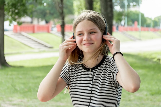 Портрет улыбающегося молодая девушка прослушивания музыки в парке