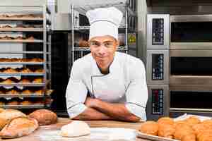 Foto gratuita ritratto di un giovane panettiere maschio sorridente in piedi dietro il tavolo con croissant freschi e pagnotta di pane