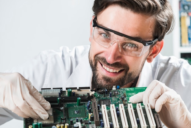 Portrait of a smiling young male technician inserting chip in computer motherboard