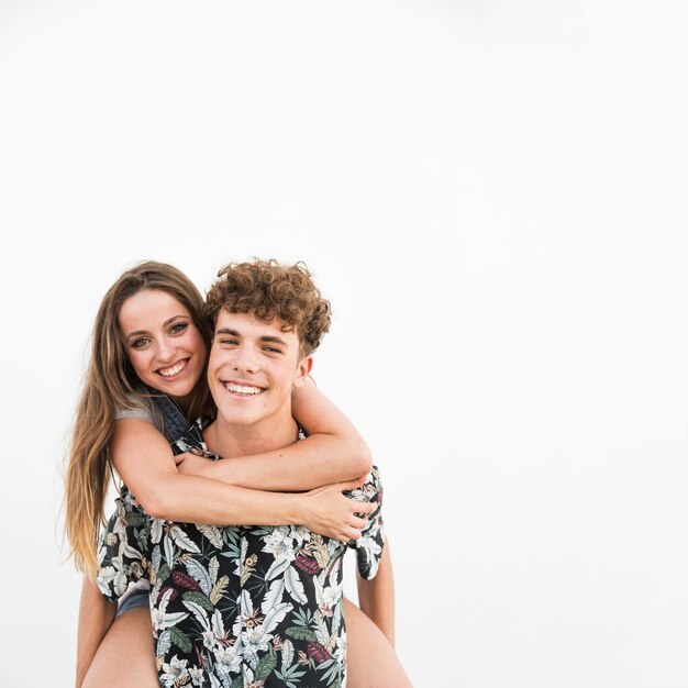 Portrait of smiling young man giving piggyback to his girlfriend on white background