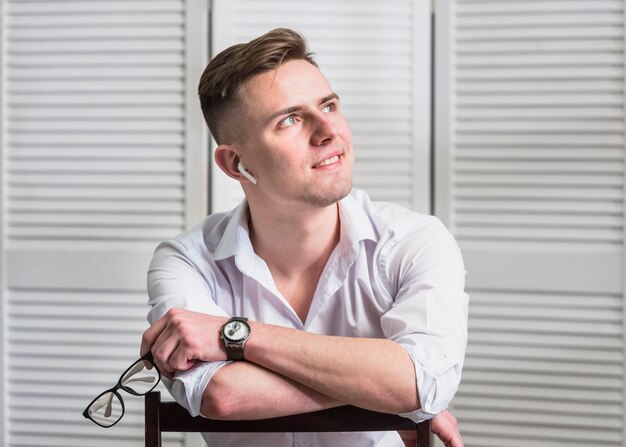 Portrait of a smiling young man holding eyeglasses in hand looking away