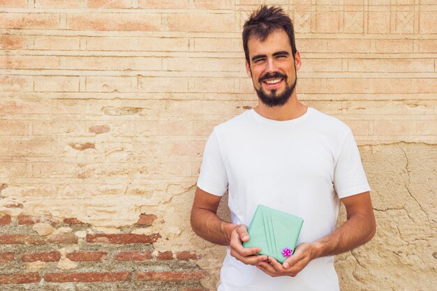 Portrait of a smiling young man holding gift against weathered wall