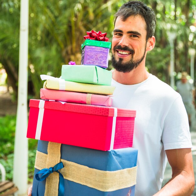 Portrait of a smiling young man holding stack of gifts