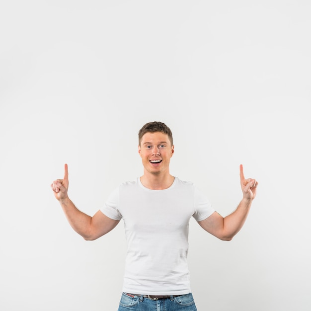 Portrait of a smiling young man pointing fingers upward against white background