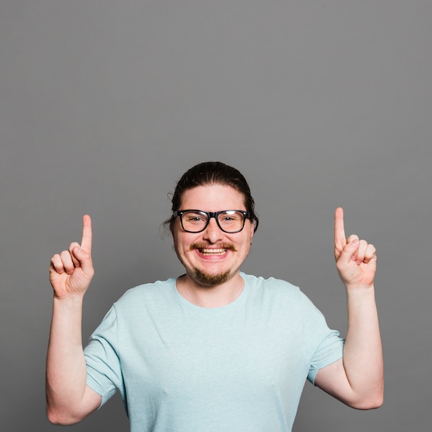 Portrait of a smiling young man pointing fingers upward looking at camera