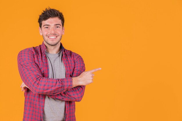 Portrait of a smiling young man pointing his finger against an orange backdrop