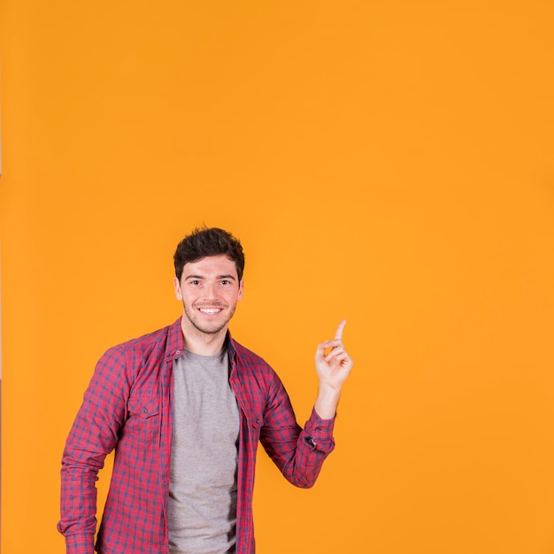 オレンジ色の背景に対して上向きに彼の指を指している笑顔の若い男の肖像