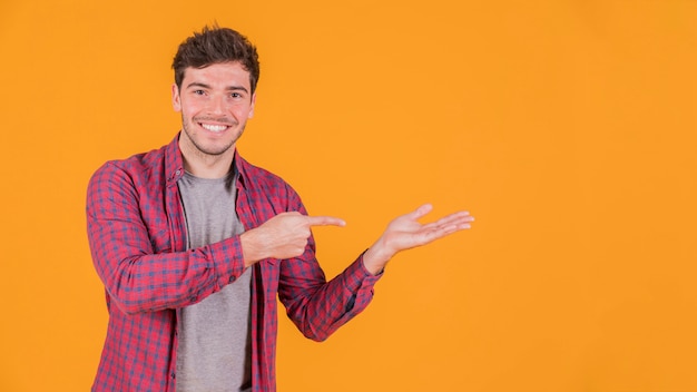 Portrait of a smiling young man pointing at something against colored backdrop
