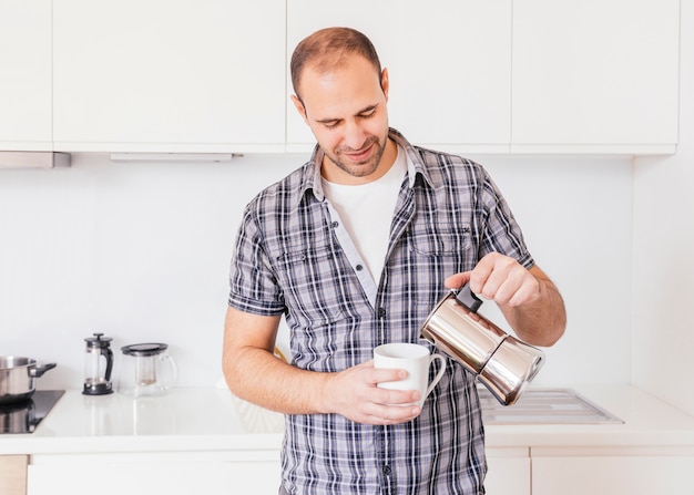 Foto gratuita ritratto di un latte di versamento sorridente del giovane nella tazza bianca