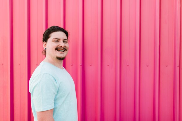ピンクの段ボールの金属板に対して立っている笑顔の若い男の肖像