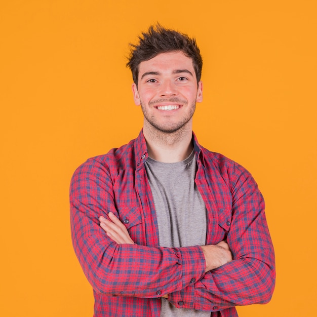 Portrait of a smiling young man with his arm crossed standing against an orange backdrop