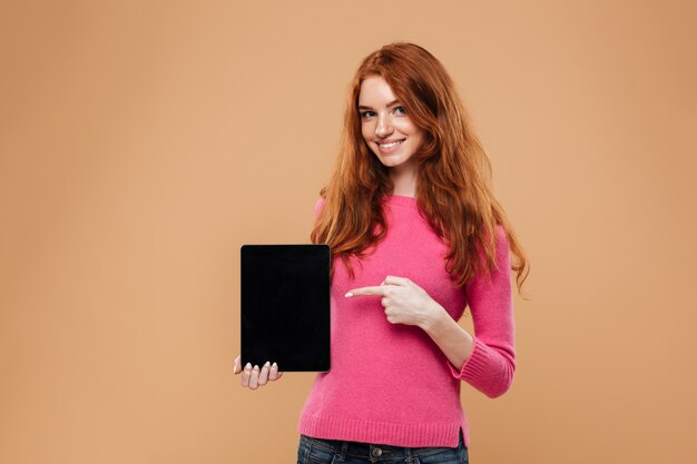 Portrait of a smiling young redhead girl pointing finger at digital tablet