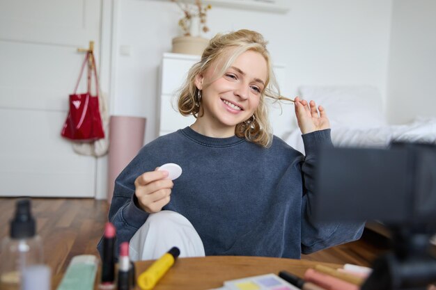 Portrait of smiling young woman applies makeup shows beauty tutorial on video records vlog on