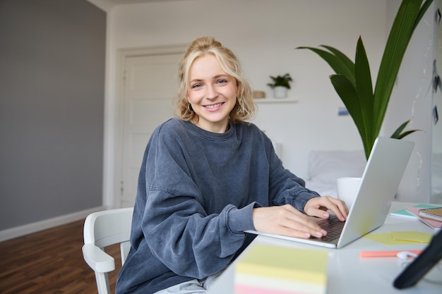 Portrait of smiling young woman college student sits in her room does homework studies remotely from