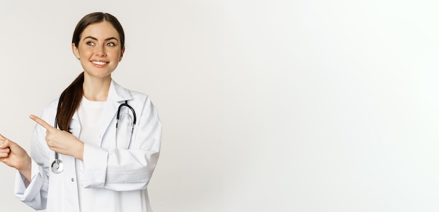 Free photo portrait of smiling young woman doctor healthcare medical worker pointing fingers left showing clini