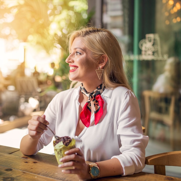 Foto gratuita ritratto di una giovane donna sorridente che mangia muffin al cioccolato nel fermacarte