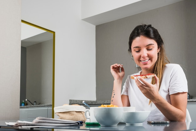 Ritratto di una giovane donna sorridente che mangia prima colazione sana a casa