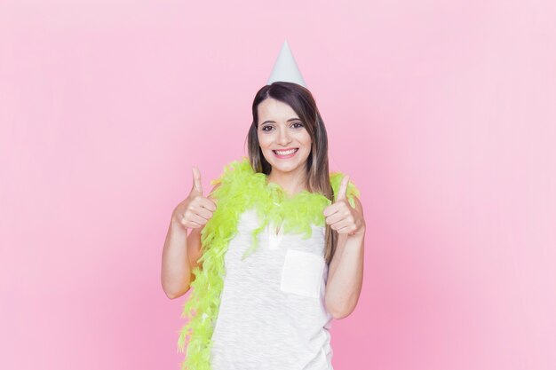 Portrait of a smiling young woman gesturing thumbs up on pink background