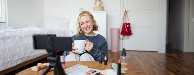 Portrait of smiling young woman girl records video on camera holds cup of tea talking doing