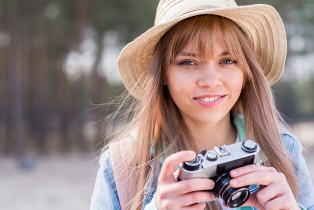 Portrait of a smiling young woman holding camera in hand looking at camera