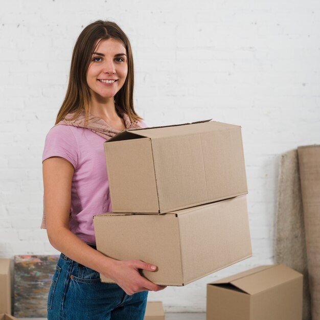 Портрет улыбающегося молодой женщины, держа в руке картонные коробки, глядя в камеру
