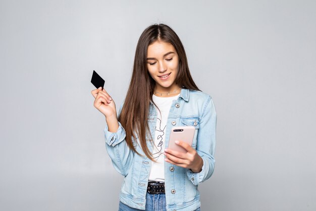 Portrait of a smiling young woman holding credit card isolated over white wall