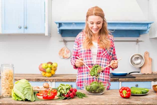 Portrait of a smiling young woman holding fresh spinach with wooden spoon