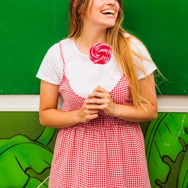 Портрет улыбающейся молодой женщины, держащей красный леденец в руке