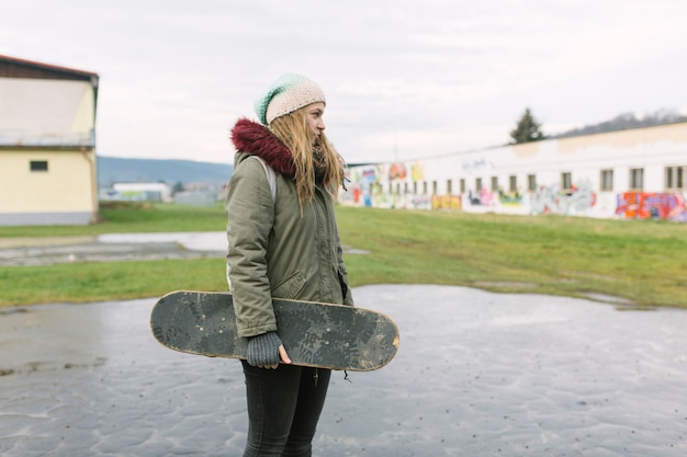 Portrait of smiling young woman holding skateboard in the park