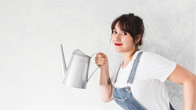 Free photo portrait of a smiling young woman holding watering can