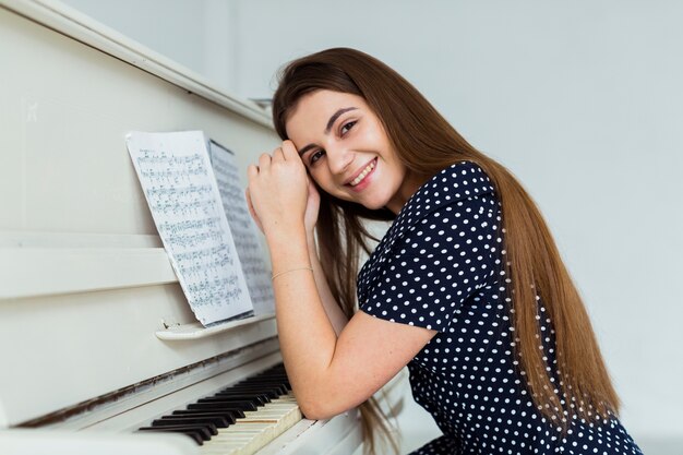 Portrait of a smiling young woman leaning on the piano looking to camera